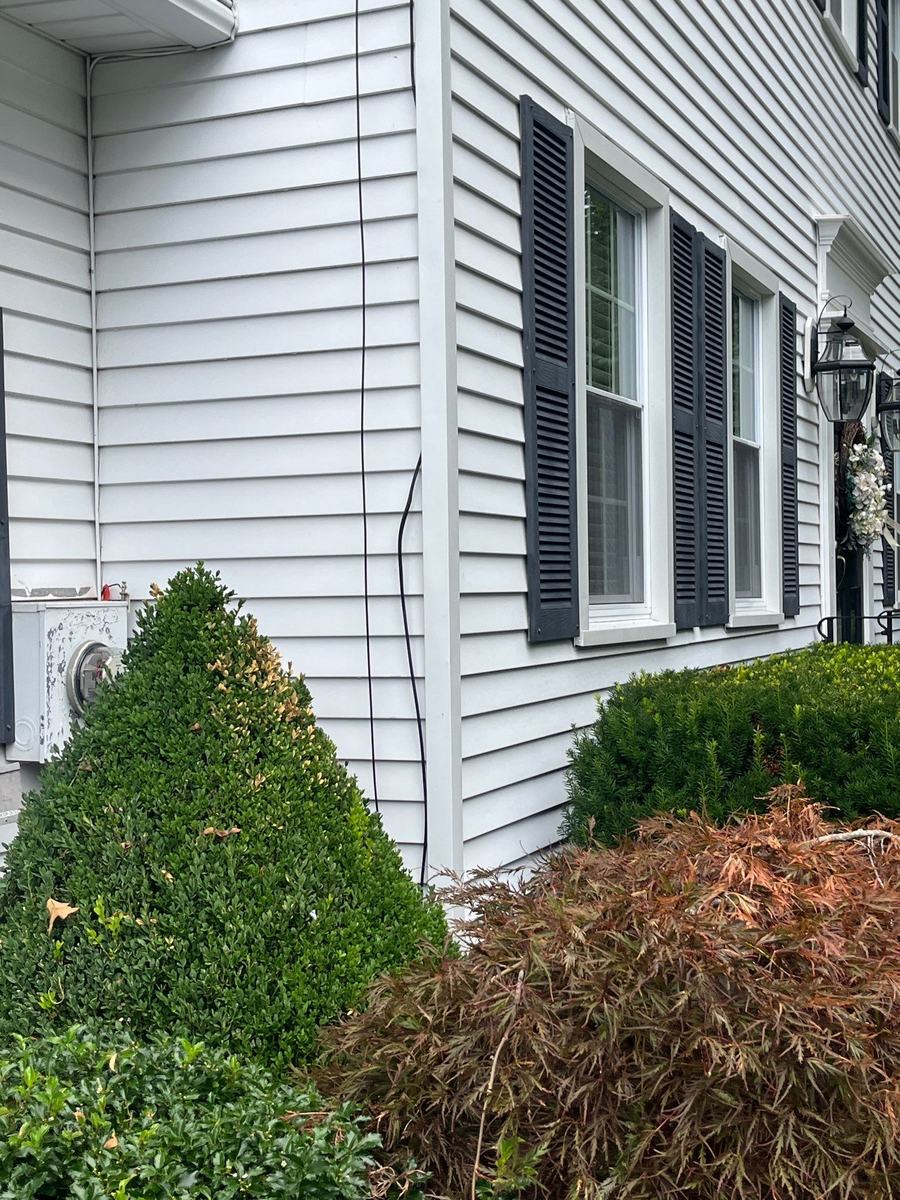 White lap siding with black louvered shutters, white window trim, and carriage lanterns beside a front entry