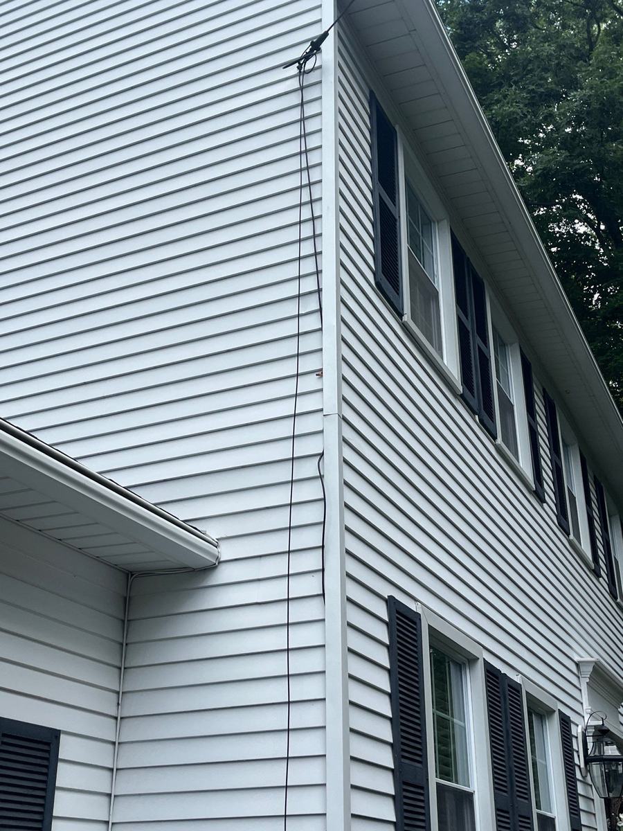 Two-storey white siding elevation meeting a gutter run and roofline at an exterior corner