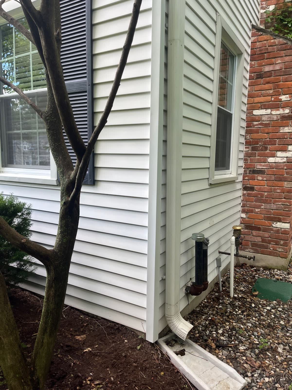 Siding corner beside windows, brick, downspout, and ground drainage