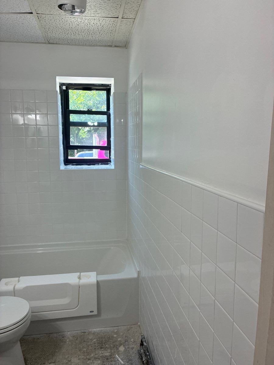 Finished white tile tub surround and wainscot tile running to a trimmed bathroom window